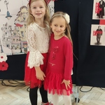 Dwie dziewczynki ubrane w biało-czerwone stroje stoją przy wystawie szkolnej.
