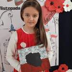 Dziewczynka ubrana w czerwoną sukienkę trzyma w ręku rysunek z Polską, w tle plakat w kolorach biało-czerwonych.