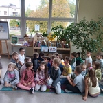 Uczniowie siedzą po turecku na dywanie, patrzą w kiernku grafiki pokazywanej przez nauczycielkę.