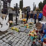 Uczniowie palą znicze w rękach przed grobem  żołnierzy.