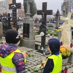 Dwóch uczniów zapala znicze przy krzyżach na cmentarzu,