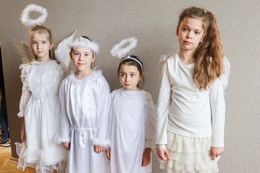 Cztery dziewczynki ubrane na biało z aureolami i skrzydłami aniołów.