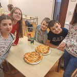 2 chłopaków i 3 dziewczyny stoją przy stole z dwiema pizzami.