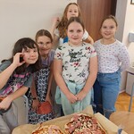 5 dziewczynek stoi przed stołem z dwiema pizzami.