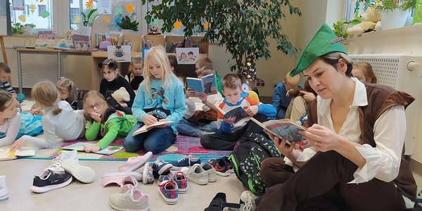 Dzieci siedzą na kolorowym dywanie i czytają książki.