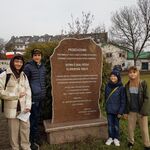 Czterech chłopców stoi przy pomniku bitwy białostockiej. W tle drzewa.