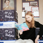 Zdjecie  dziewczyny czytającej książkę. Dziewczyna siedzi na kwadratowych pufach.