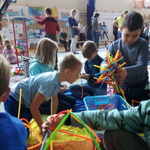 Grupa dzieci siedzi przy zabawkach i układa kolorowe patyczki 