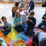 Grupa dzieci siedzi przy zabawkach i układa kolorowe patyczki 