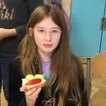 Dziewczynka z długimi włosami trzyma w prawej ręce kanapkę.