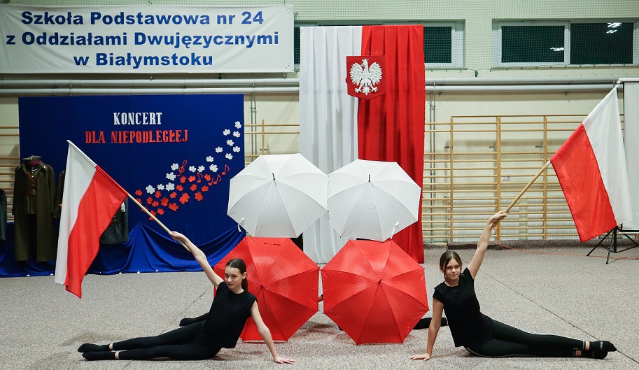 Dwie dziewczyny trzymają flagi polskie za nimi parasole w barwach biało-czerwonych