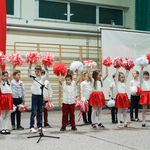 Na sali gimnastycznej stoją uczniowie ubrani w barwy biało-czerwone , w rękach trzymają pompony w kolorach biało-czerwonych.