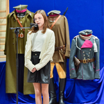 Dziewczynka stoi przed mikrofonem, w tle widać mundury żołnierskie.