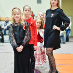 Kobieta ubrana w czarną sukienkę stoi obok dzieci ubranych w barwy biało-czerwone
