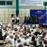 Zdjęcie uczniów zgromadzonych na apelu na sali gimnastycznej. Wszyscy ubrani w barwach biało-czarnych.
