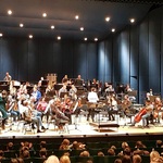 Muzycy z instrumenatmi siedzą na scenie opery.
