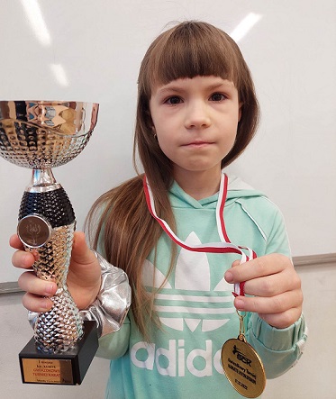 Zdjęcie dziewczynki, która trzyma puchar i medal w rękach.