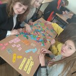 Uczennice siedzą w szkolnych ławkach i układają kolorowe puzzle z angielskimi słówkami.
