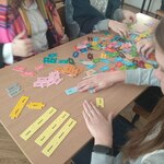 Uczennice siedzą w szkolnych ławkach i układają kolorowe puzzle z angielskimi słówkami.