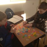 Uczniowie siedzą w szkolnych ławkach i układają kolorowe puzzle z angielskimi słówkami.