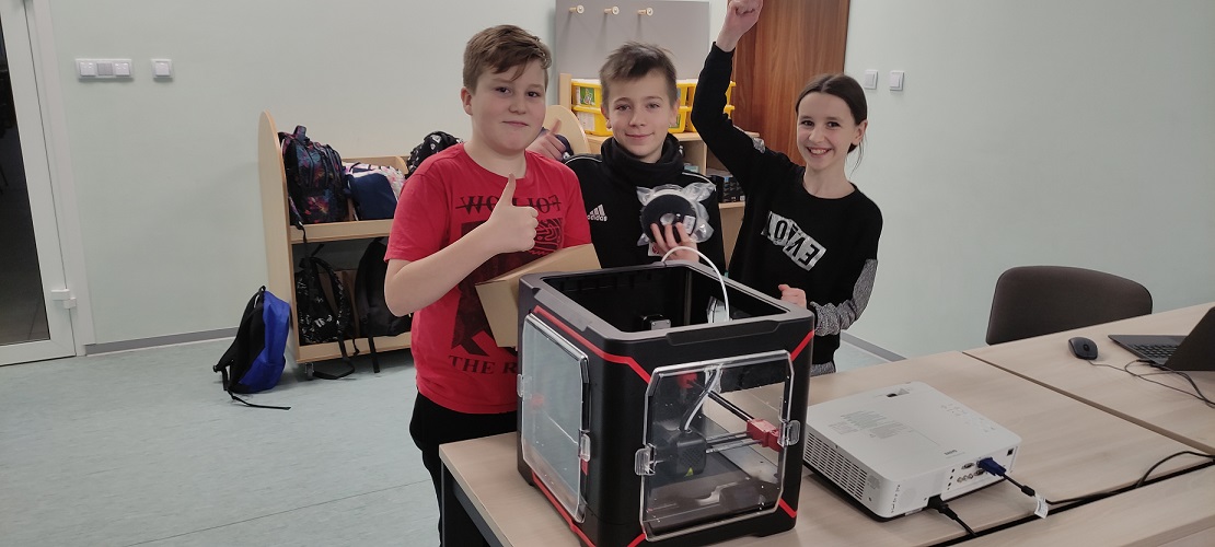 3 uczniów stoi przy drukarce 3D