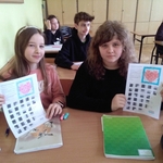 Dziewczynki siedzą w ławce szkolnej i trzymają w rękach kartki z sercami i łamigłówkami.jpg