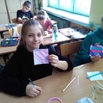 Dziewczynki siedzą w ławce szkolnej i trzymają w rękach kartki z sercami..jpg
