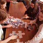 Uczennice układają na stole duże puzzle - banknoty.