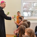 Arcybiskup wręcza kwiaty uczennicy, obok siedzą uczniowie.
