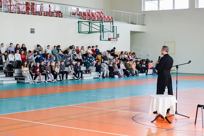 Misjonarz przemawia do uczniów siedzących na trybunach.