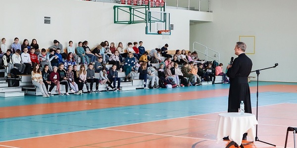Misjonarz przemawia do uczniów siedzących na trybunach.