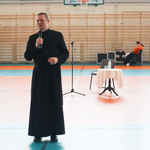 Misjonarz przemawia do uczniów na hali sportowej.