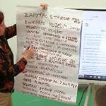 Pani edukatorka pokazuje informacje zapisane na dużym arkuszu papieru.