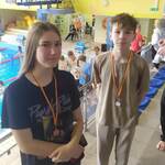 Uczeń i uczennica z medalami na szyi, w tle widok basenu.