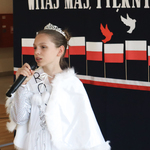 Dziewczynka ubrana na biało mówi do mikrofonu. W tle patriotyczny napis.
