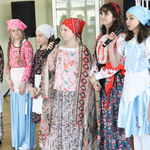 Grupa dziewczynek przebrana w stroje ludowe trzyma w ręku mikrofony lub mówi do nich.