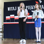 Dwie dziewczynki mówią do mikrofonu. W tle patriotyczny napis.