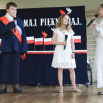 Dwie dziewczynki oraz chłopiec mówią do mikrofonu. W tle patriotyczny napis.