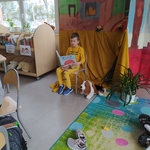 Chłopiec siedzi na krześle na tle kolorowej scenografii_ czyta książkę_ obok leży pies- maskotka..jpg