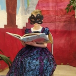 Dziewczynka przebrana w suknię księzniczki oraz z maską na twarzy czyta książkę..jpg