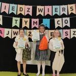 Trzy dziewczynki stoją na tle kolorowego napisu i trzymaja w rękach dyplomy..jpg