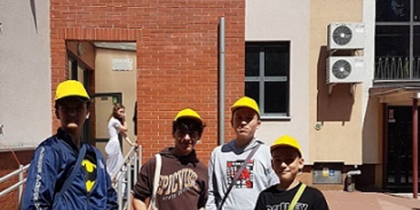 Czterech uczniow stoi w żółtych czapkach na tle liceum katolickiego..jpg