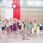 Dzieci ubrane w kolorowe i wakacyjne stroje wsytępują na sali gimnastycznej.