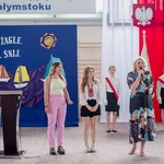 Pani dyretkor przemawia przez mikrofon. Obok stoją dwie wolontariuszki