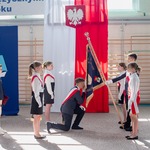 Uczniowie ubrani na galowo przekazują sztandar szkoły.