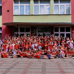 Duża grupa uczniów ubrana na czerwono wraz z nauczycielami pokazuje z dłoni serduszka.