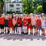 Grupa dzieci ubranych w czerwone w koszulki stoi na podwórku.