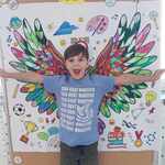 Chłopiec stoi na tle plakatu z kolorowymi skrzydłami..jpg