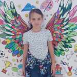 Dziewczynka stoi na tle plakatu z kolorowymi skrzydłami..jpg