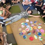 Grupa uczniów siedzi na dywanie obok szarego papieru z kolorowymi kropkami..jpg